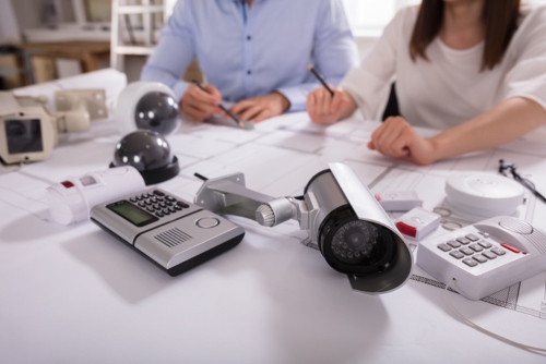 Various Security Equipments In Front Of Two People Planning Project On Blueprint